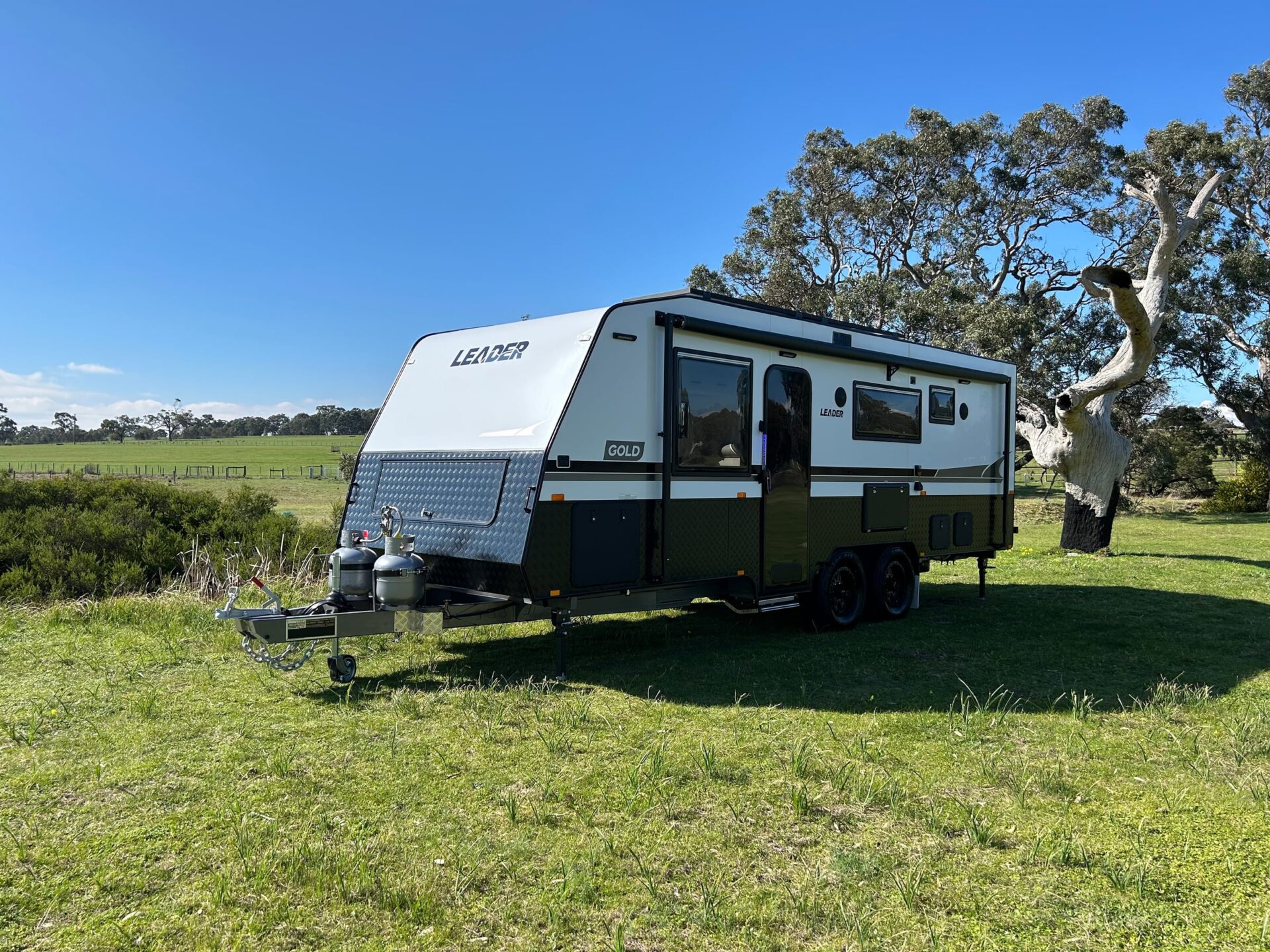 Leader Gold LE caravan exterior — driver-side profile with awning extended over entry door showing Leader Gold decals