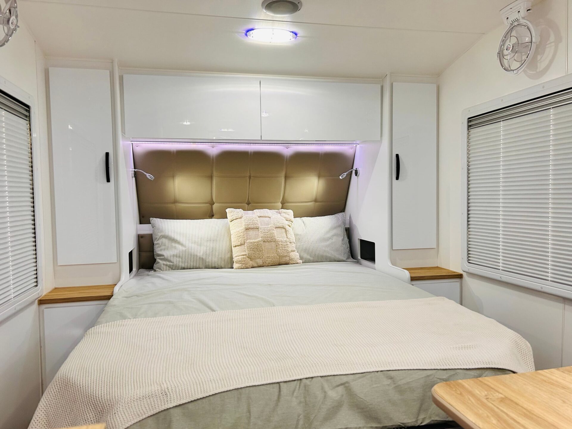 Leader Gold LE caravan interior — island queen bed with padded buttoned headboard and LED accent strip lighting