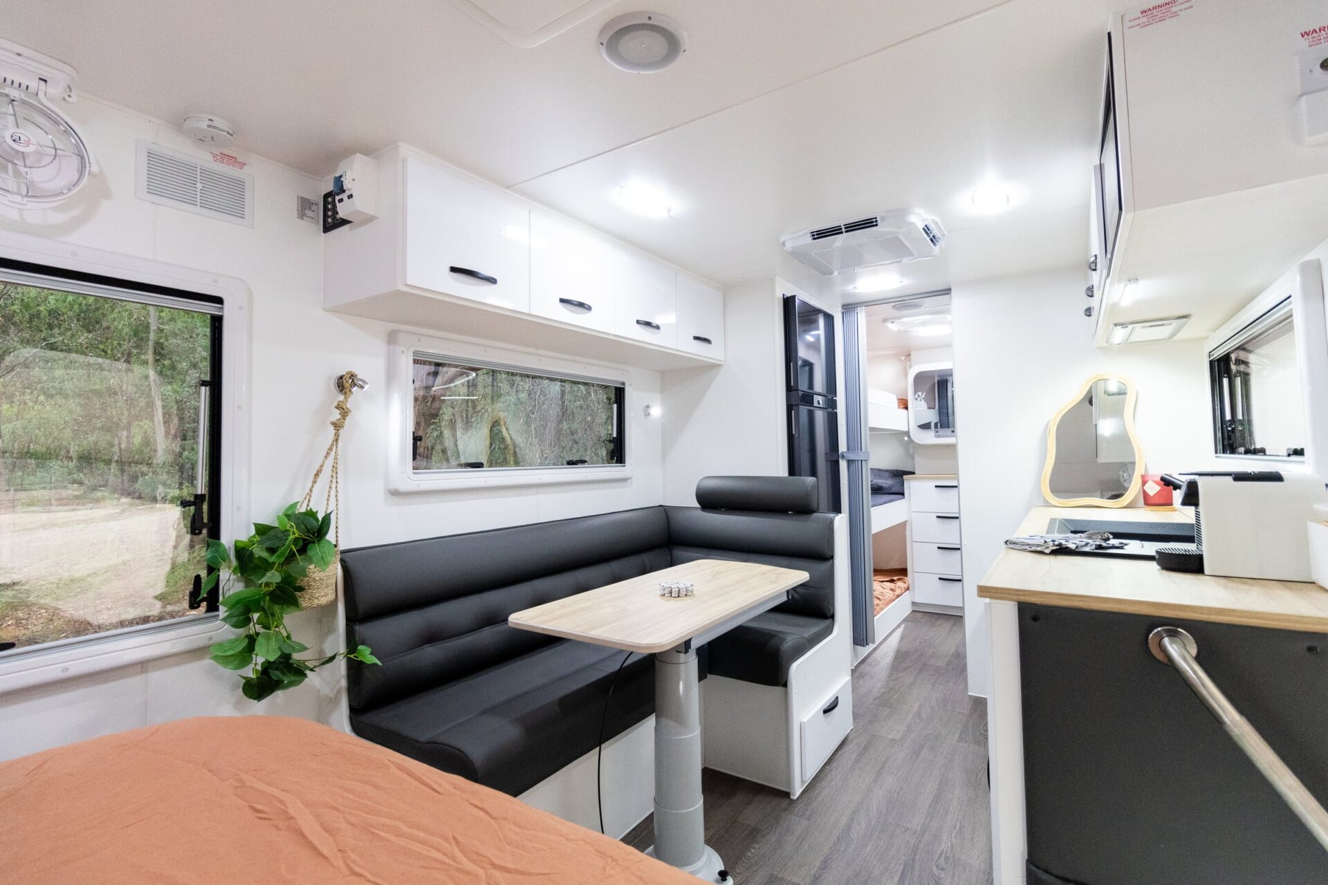Leader Gold LE caravan interior — L-shaped black leather dinette with timber-look table looking through to bunks and kitchen at rear