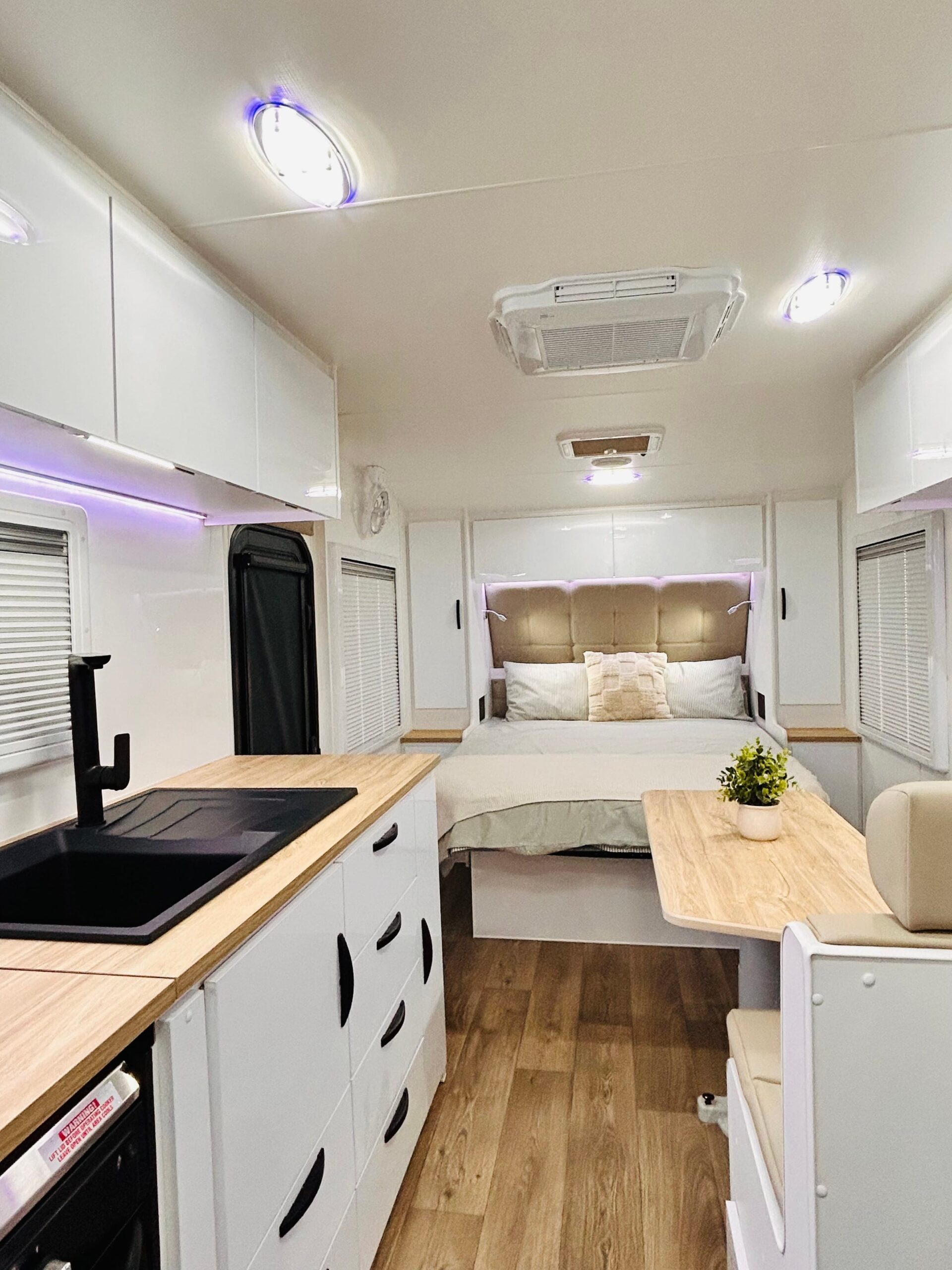 Leader Gold LE caravan interior — full-length view from kitchen with black granite sink and timber benchtop through to bedroom