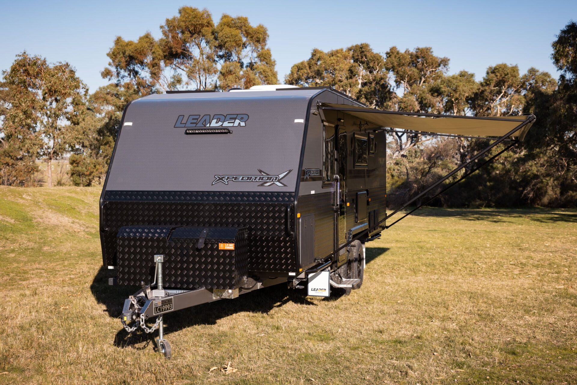 Leader Xpedition caravan exterior — front three-quarter driver-side view with black checker-plate cladding, Leader Xpedition decals and stone guard
