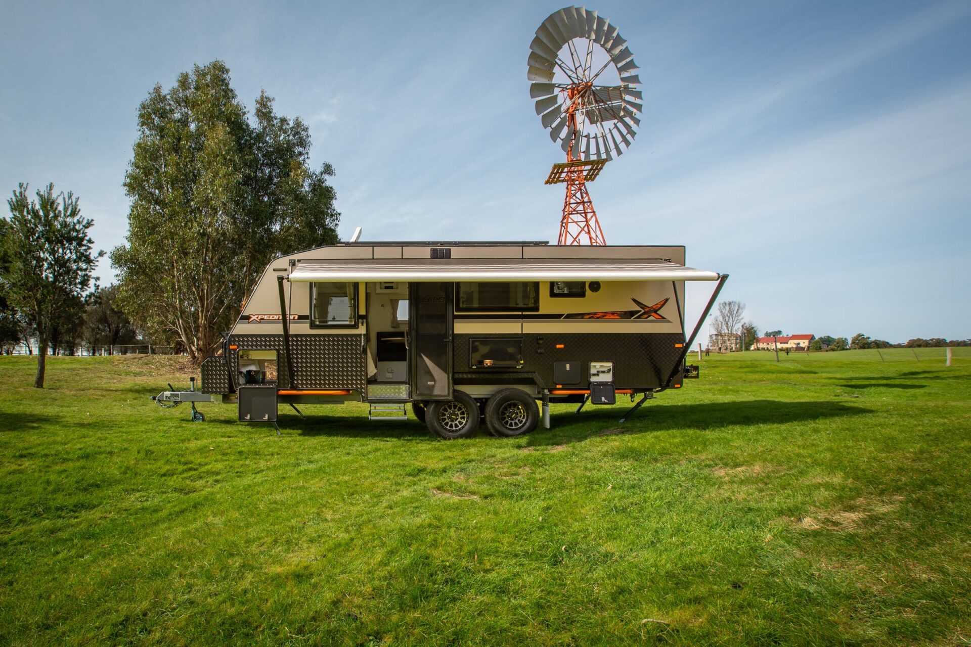Leader Xpedition caravan exterior — full passenger-side profile with tandem alloy wheels, full-length awning extended, pull-out step and external slide-out kitchen