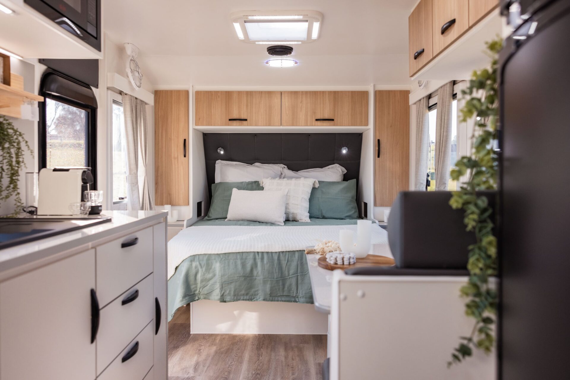 Leader Xpedition caravan interior — L-shaped leather dinette with white stone kitchen, sink, oven and drawers looking through to ensuite at rear