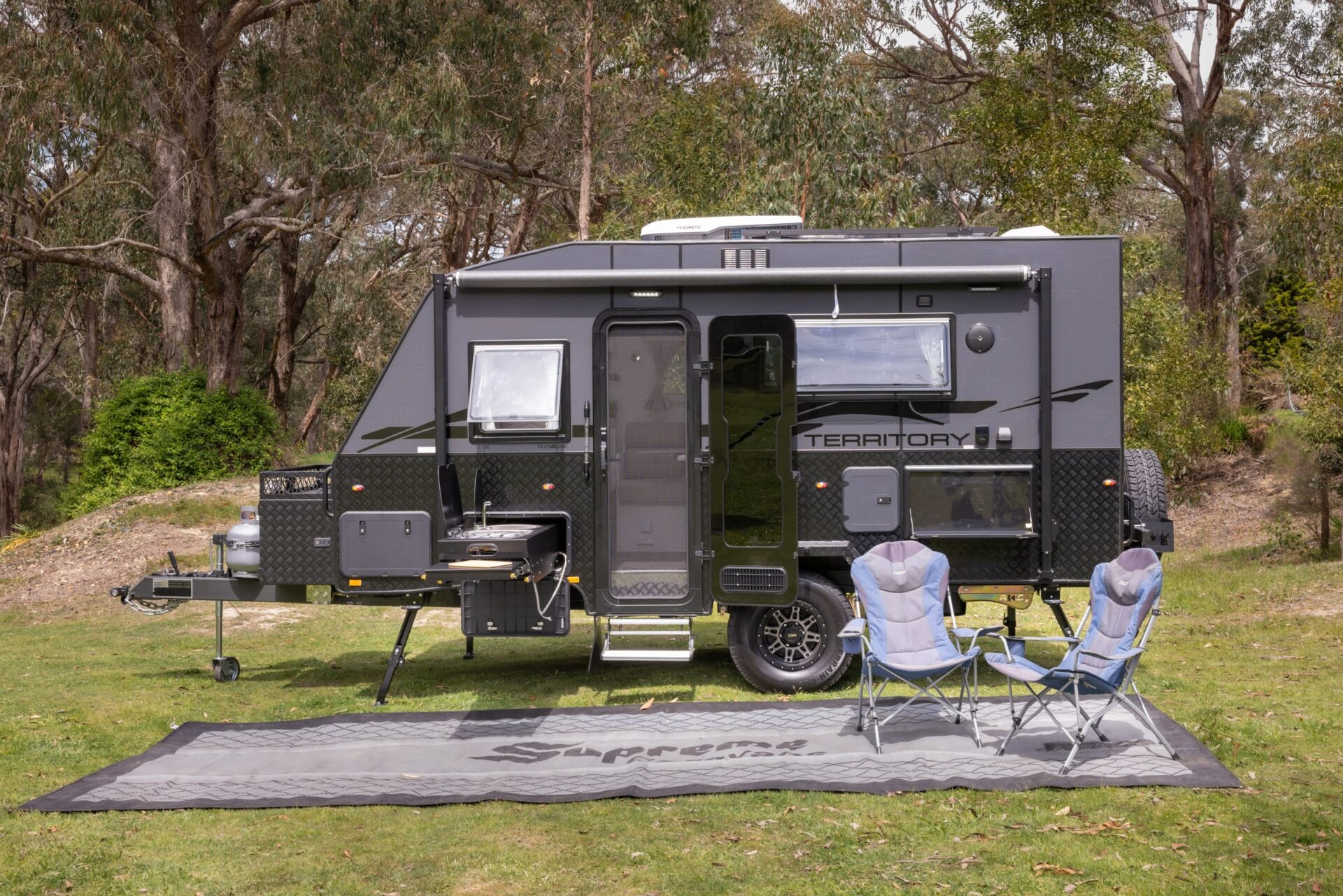 Supreme Territory at a bush campsite — twin gas bottles, jockey wheel, slide-out outdoor kitchen, awning and Supreme branded mat